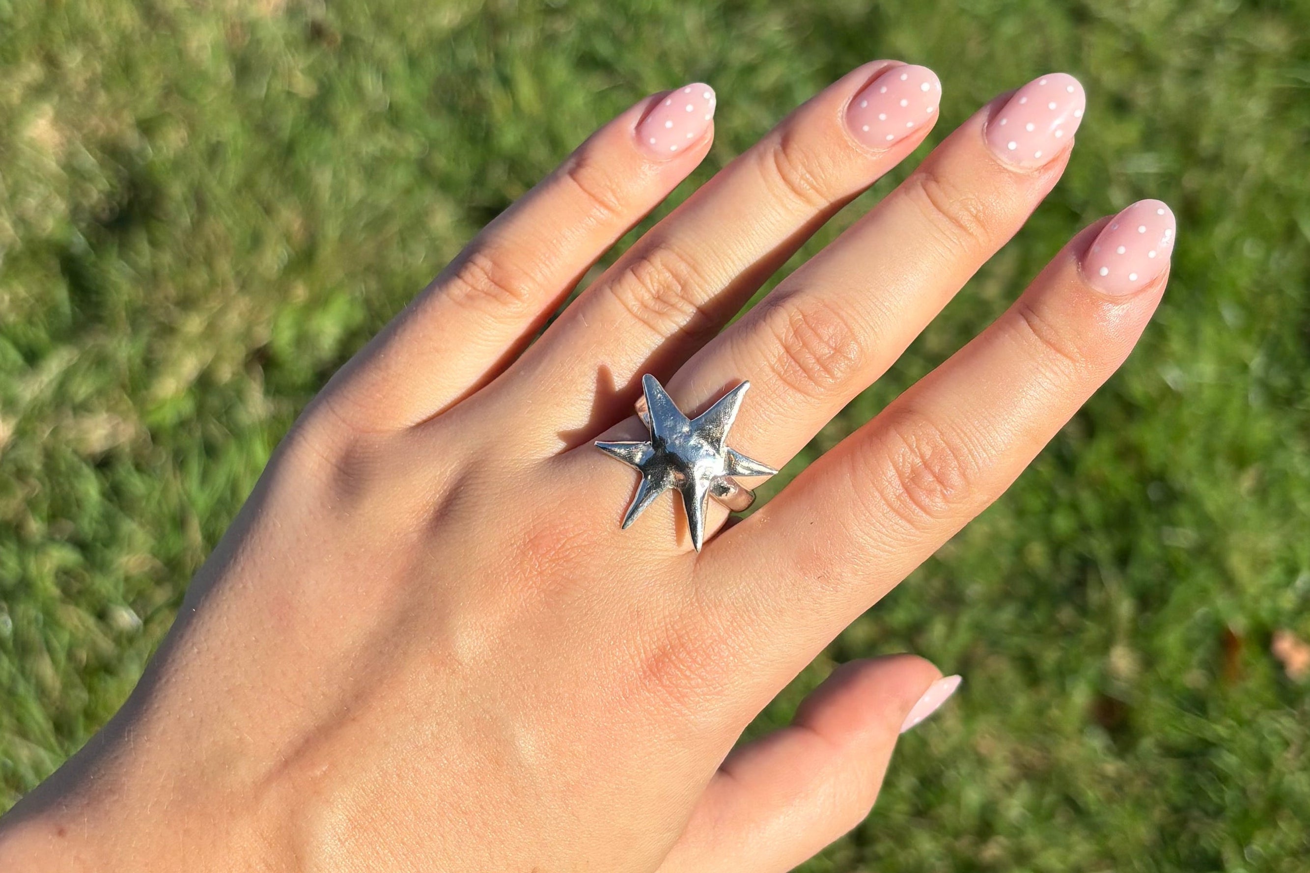 Hand wearing a star-shaped ring on a grassy background