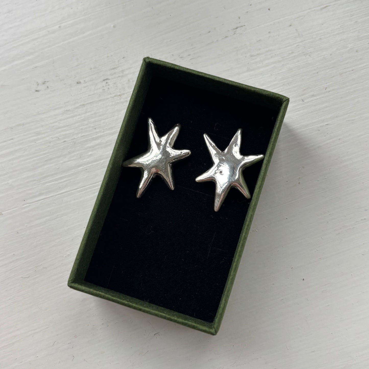 Silver star-shaped earrings in a black box on a white surface