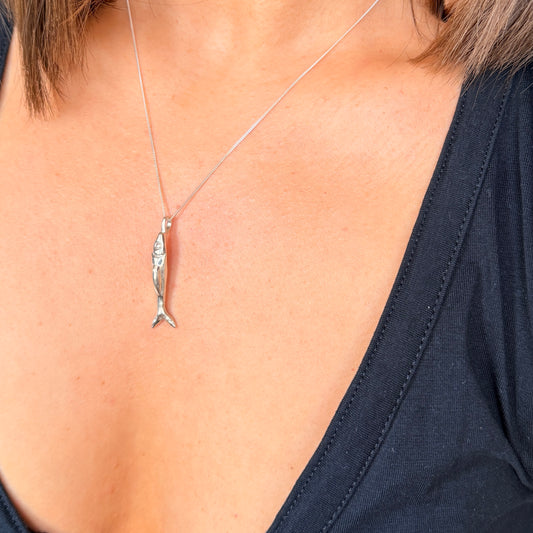 Silver fish pendant necklace on a person wearing a dark blue top.