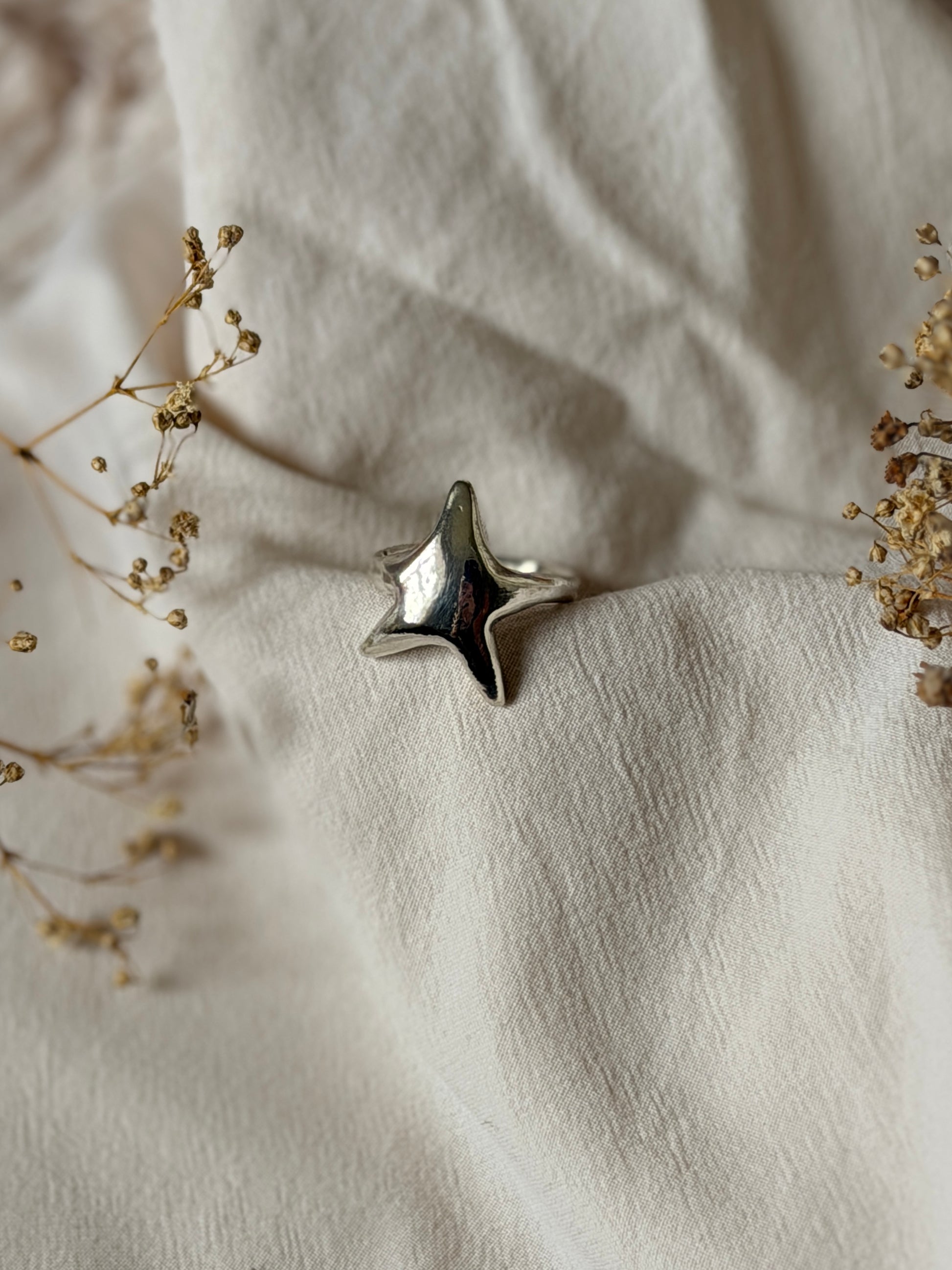 Silver star-shaped ring on a textured beige fabric background