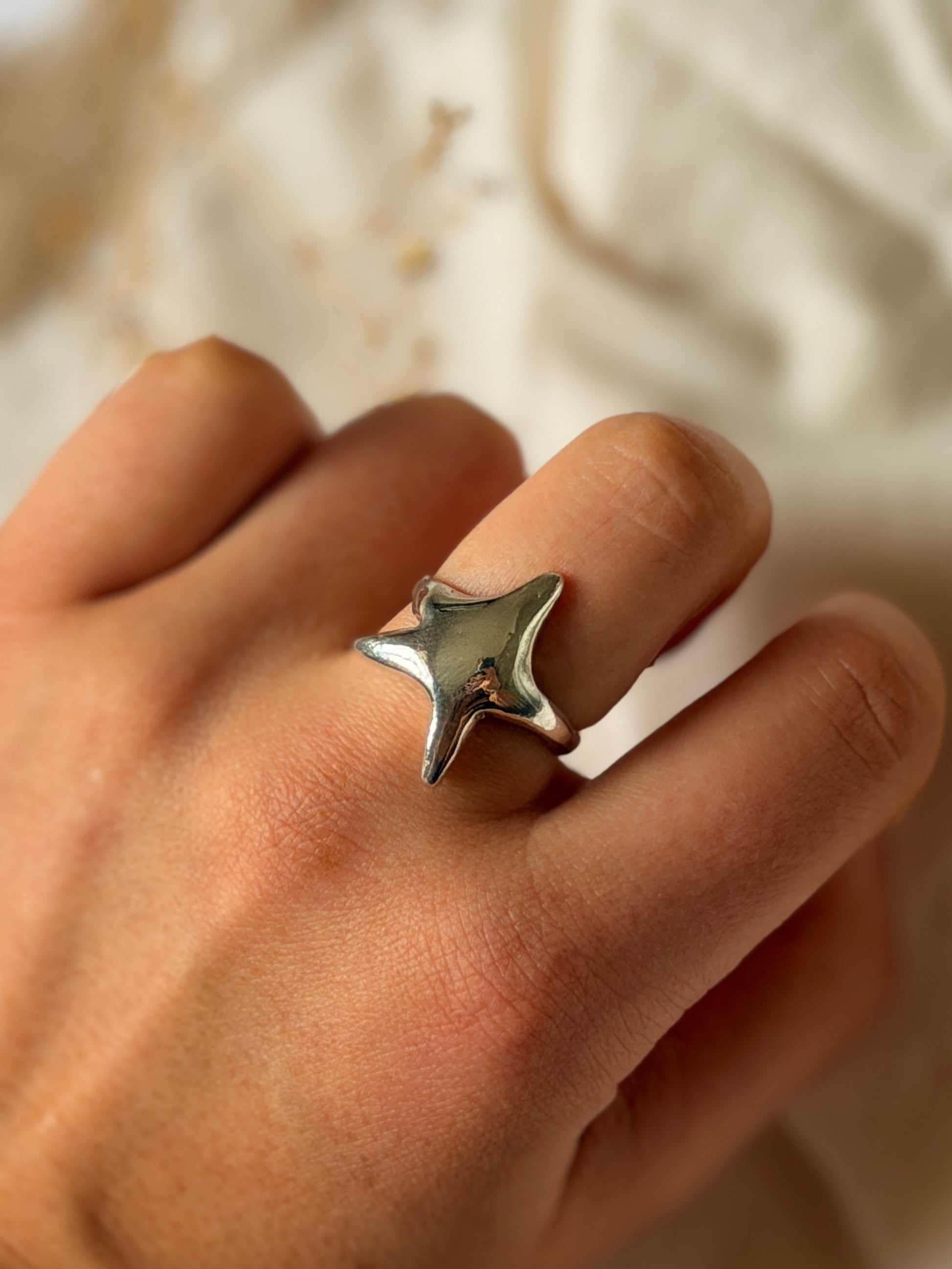 Silver star-shaped ring on a person's finger with a soft background