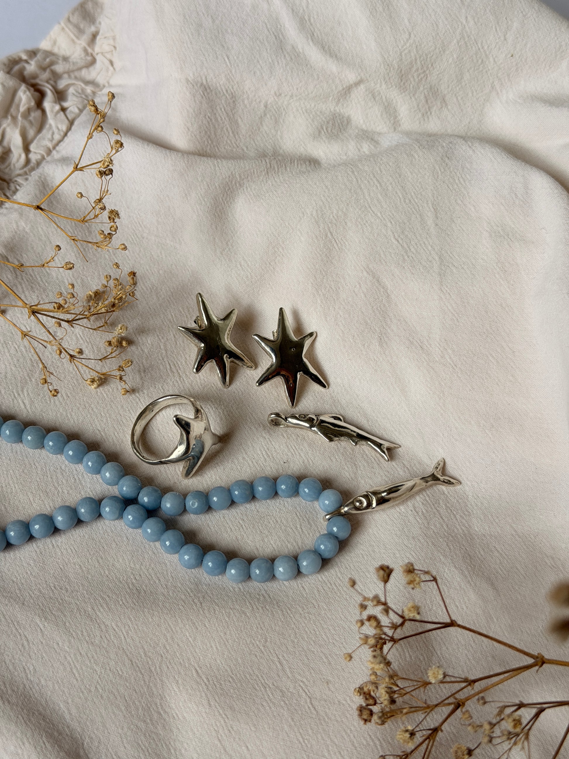 Jewelry set with star-shaped earrings and a blue beaded necklace on a textured surface with dried flowers.