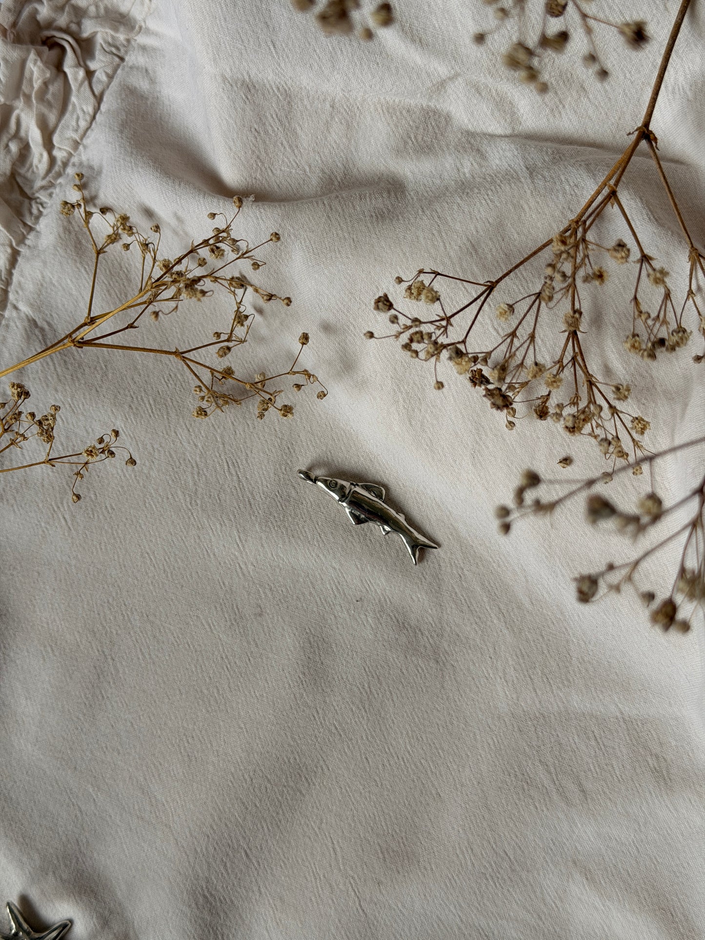 Small fish figurine on a textured white surface with dried flowers.
